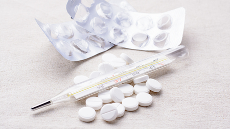 Thermometer and pills scattered on a napkinの写真素材