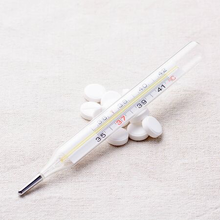 Thermometer and pills scattered on a napkinの写真素材