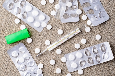 Thermometer and pills scattered round on sackingの写真素材
