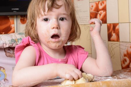 Frightened little girl sitting at a table and playing with the doughの写真素材