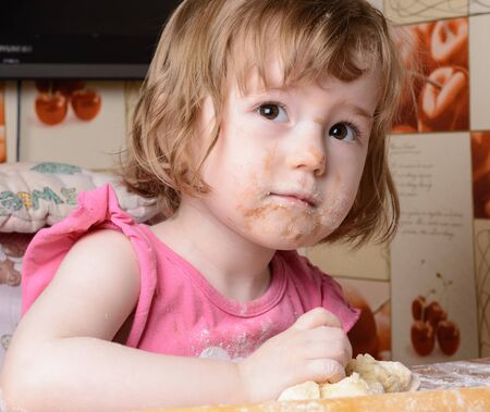 Frightened little girl sitting at a table and playing with the doughの写真素材