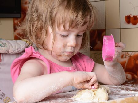 Frightened little girl sitting at a table and playing with the doughの写真素材