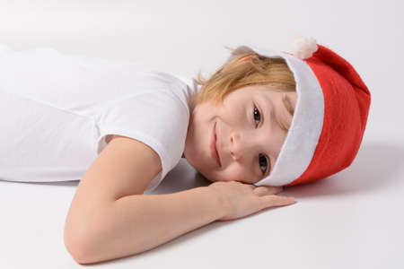 Little girl in santa hat lying on the white floorの写真素材