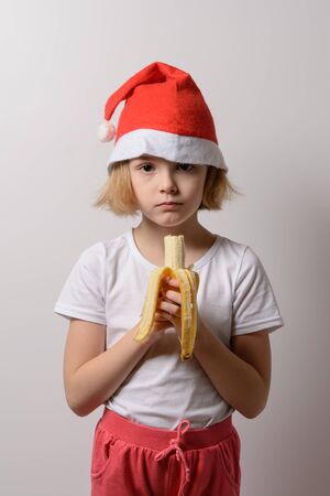 Little girl in santa hat eating a bananaの写真素材