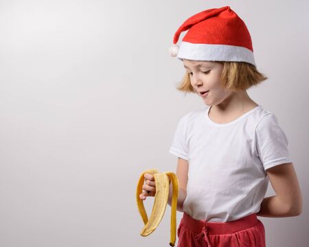 Little girl in santa hat eating a bananaの写真素材