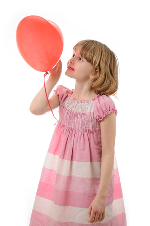 Little girl in a pink dress holding a red balloon in the shape of a heart on a white backgroundの写真素材