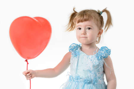 Little girl in a blue dress holding a red balloon in the shape of a heart on a white backgroundの写真素材