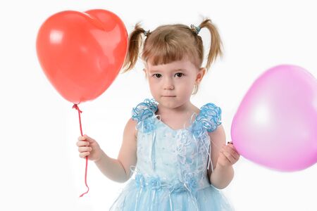 Little girl in a blue dress holding a red balloon in the shape of a heart on a white backgroundの写真素材