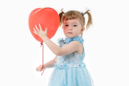 Little girl in a blue dress holding a red balloon in the shape of a heart on a white backgroundの写真素材