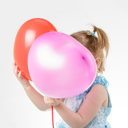 Little girl in a blue dress holding a red balloon in the shape of a heart on a white backgroundの写真素材