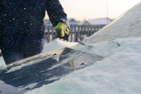 Male green brush cleans snow from carの写真素材