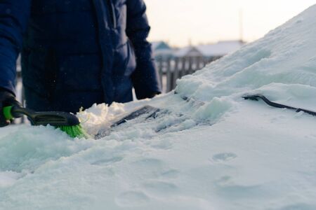 Male green brush cleans snow from car