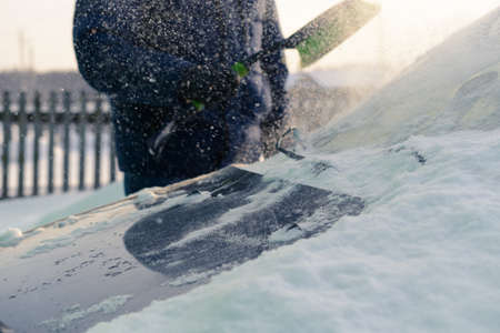 Male green brush cleans snow from carの写真素材