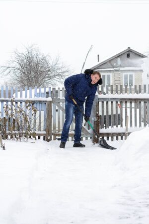 Young man in a blue jacket removes snow shovel in the yard of a blackの写真素材