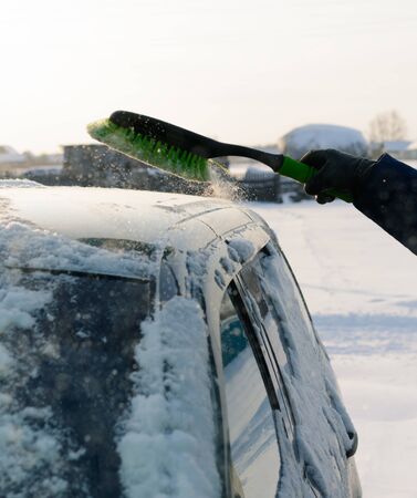Male green brush cleans snow from carの写真素材