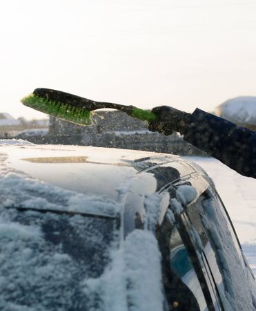 Male green brush cleans snow from carの写真素材