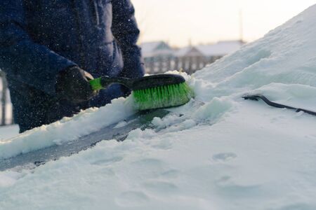 Male green brush cleans snow from carの写真素材