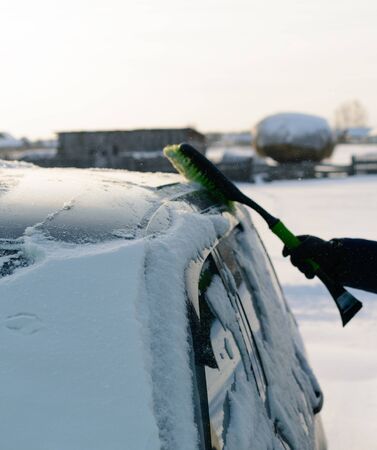 Male green brush cleans snow from carの写真素材