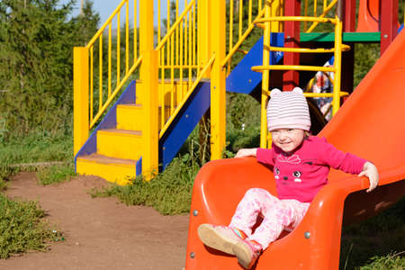 Little girl in a pink hat is riding a roller coaster at the playgroundの写真素材