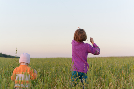 Two girls standing back flying their kite in a fieldの写真素材