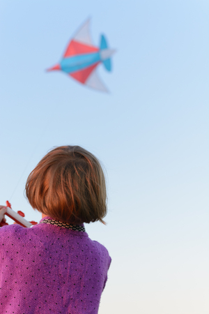 Girl in a purple jacket runs a kite in a fieldの写真素材