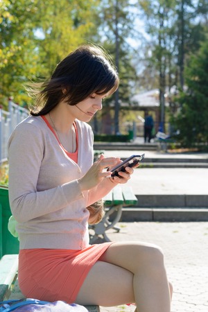 Girl brunette sitting in the park in the summer with the phoneの写真素材