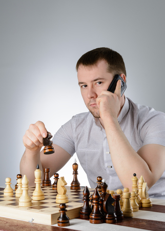 A man in a white shirt and thinks with the phone over a game of chessの写真素材