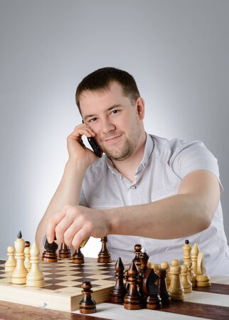 A man in a white shirt and thinks with the phone over a game of chessの写真素材