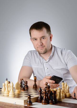 A man in a white shirt and thinks with the phone over a game of chessの写真素材
