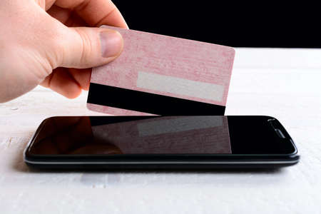 Man's hand holds a credit card on the screen smartphone