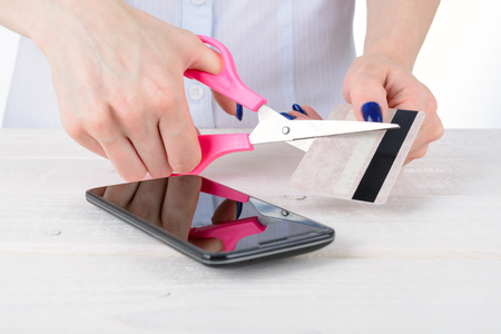 Girl with scissors cuts the credit card over the phoneの写真素材