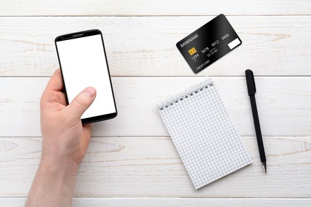 Smartphone, notebook, pen and credit card on a white wooden table