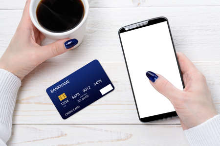A woman sitting at a white wooden table and pay for purchases via smartphoneの写真素材