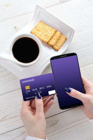 A woman sitting at a white wooden table and pay for purchases via smartphoneの写真素材