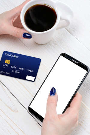 A woman sitting at a white wooden table and pay for purchases via smartphoneの写真素材