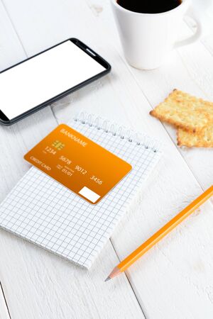 Smartphone, notebook, pencil and credit card on a white wooden tableの写真素材