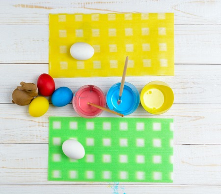 Chicken eggs and paint with brushes lie on a white wooden tableの写真素材
