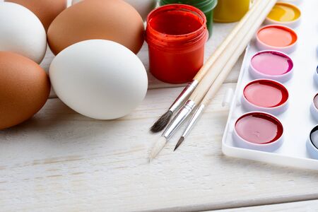 Chicken eggs and paint with brushes lie on a white wooden tableの写真素材