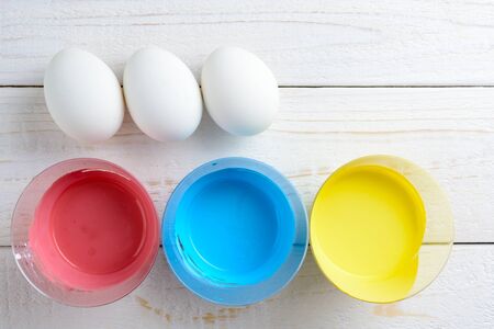 Chicken eggs and paint lie on a white wooden tableの写真素材