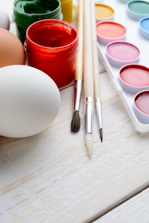 Chicken eggs and paint with brushes lie on a white wooden tableの写真素材