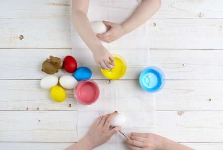Children paint eggs for Easter on a wooden table top viewの写真素材