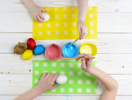 Children paint eggs for Easter on a wooden table top viewの写真素材
