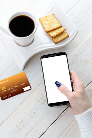 A woman sitting at a white wooden table and pay for purchases via smartphoneの写真素材