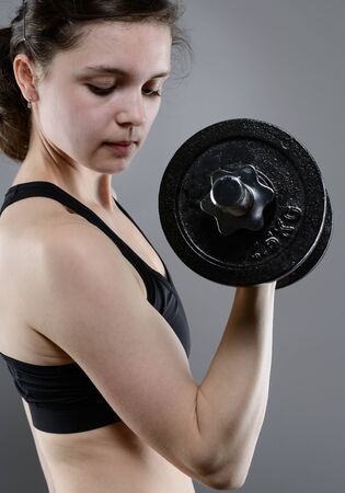 Young woman in sportswear lifting heavy dumbbellsの写真素材