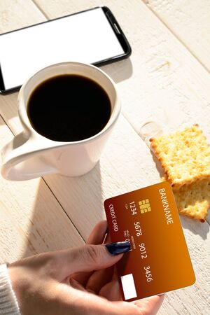 A woman sitting at a white wooden table and pay for purchases via smartphoneの写真素材