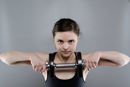 Young woman in sportswear lifting heavy dumbbells