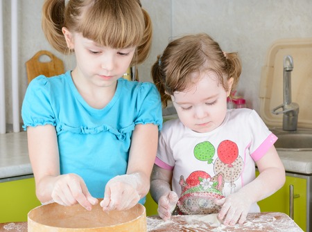 Two sisters sifts the flour to the dough in the kitchenの写真素材