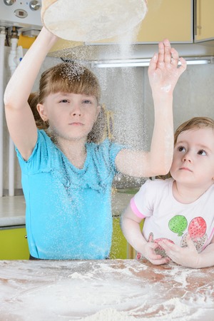 Two sisters sifts the flour to the dough in the kitchenの写真素材