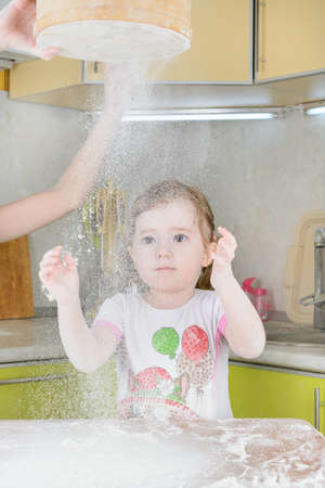 Little girl sifts the flour for the doughの写真素材