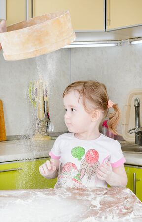 Little girl sifts the flour for the doughの写真素材